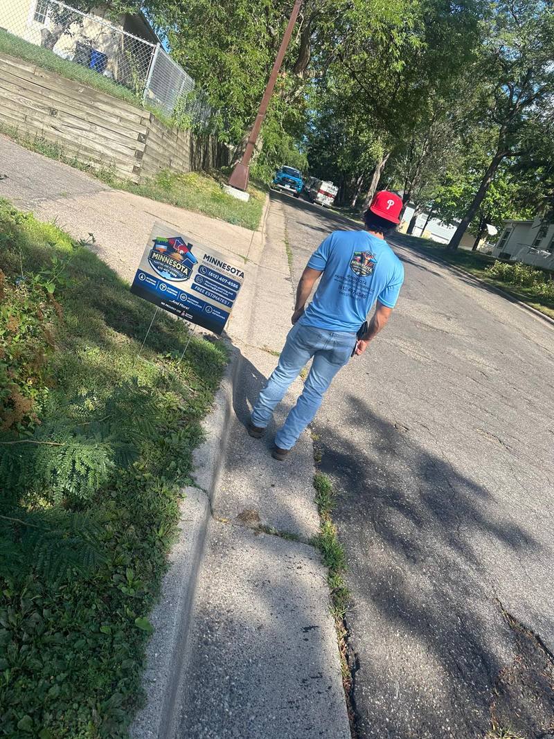 A crew member walking a St Paul sidewalk carrying the company yard sign